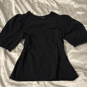 Svart blus med puffärmar - Snygg svart blus med puffiga trekvartsärmar. Perfekt för en stilren look. Tillverkad i ett mjukt material som ger en bekväm passform.