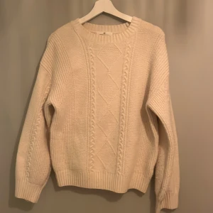 Vit stickad tröja från H&M - Säljer en mysig vit stickad tröja från H&M med ett snyggt flätmönster på framsidan. Tröjan har långa ärmar och ribbade muddar vid ärmslut och nederkant. Perfekt för kyliga dagar!
