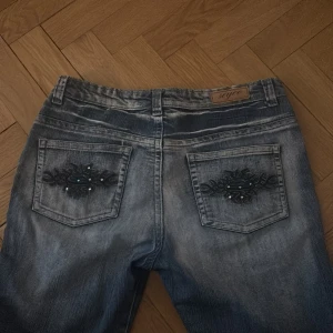 Snygga baggy jeans med fina detaljer - Snygga blå jeans från SWAG med unika broderade detaljer på bakfickorna. Jeansen har en klassisk femficksdesign och är dekorerade med diamanter. Skulle säga att storleken passar M/L. Pris kan diskuteras vid snabb affär❤️