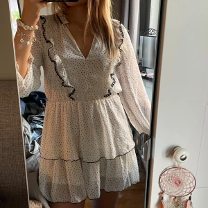 Vit prickig klänning från Zara - Säljer en söt vit klänning från Zara med svarta prickar och volangdetaljer. Så fin för sommaren och avslutningar!