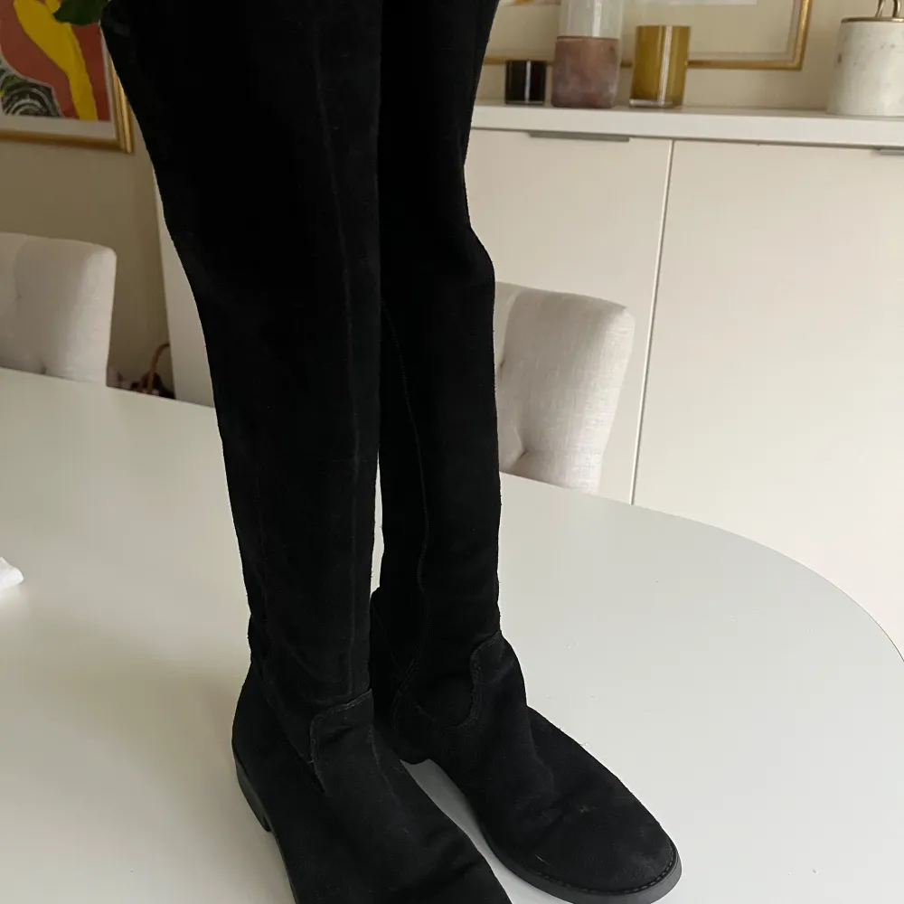 Snygga svarta stövlar i mocka med dragkedja på sidan. Perfekta för höst och vinter, dessa stövlar har en klassisk design som passar till många olika outfits.. Kengät.