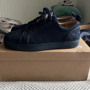 Louboutin Mörkblå - Snygga mörkblå Louboutin i mocka med broderad text på hälen. Skorna har en klassisk design med snörning och en bekväm innersula. Perfekta för en stilren look.