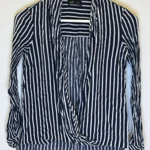 Randig blus från TRF Zara - Snygg randig blus från TRF i mörk blå och vit. Blusen har långa ärmar och en öppen design framtill. Perfekt för en stilren look. Den behöver bara strykas. 