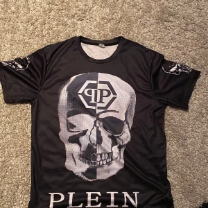 Philipp plein T-shirt  - Cool svart t-shirt från Plein med stort dödskalletryck på både fram- och baksida. Material påminner om tränings tröja.                                                                                       Har ingen philipp plein tag                                                        Sitter större i storleken 