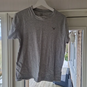 Grå t-shirt från GANT - Säljer en stilren grå t-shirt från GANT. Den är kortärmad och har en liten broderad logga på bröstet. Perfekt för en avslappnad look.