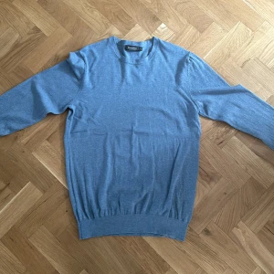 Blå tröja från Dressmann - Säljer en snygg blå tröja från Dressmann i Supima bomull. Perfekt för både vardag och lite finare tillfällen. Tröjan har en normal passform och långa ärmar, vilket gör den idealisk för höst och vår. Den är i bra skick och superbekväm att ha på sig.