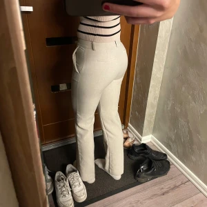 Kostymbyxor  - Beiga kostymbyxor ifrån Nelly i storlek 32. Jag är 172 cm lång och bär storlek S. En knapp saknas men det går att stänga ändå eftersom de har de två metall ”knapparna” på