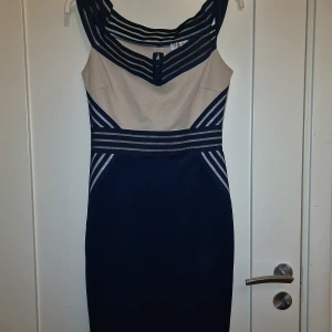 Elegant klänning i beige och marinblå - Säljer en superfin klänning i beige och marinblå med ett unikt randigt mönster vid halsen och midjan som framhäver figuren. Den är i storlek 40. Perfekt för festliga tillfällen eller en fin middag. Mycket bekväm och i bra skick! Pris: 299 kr.