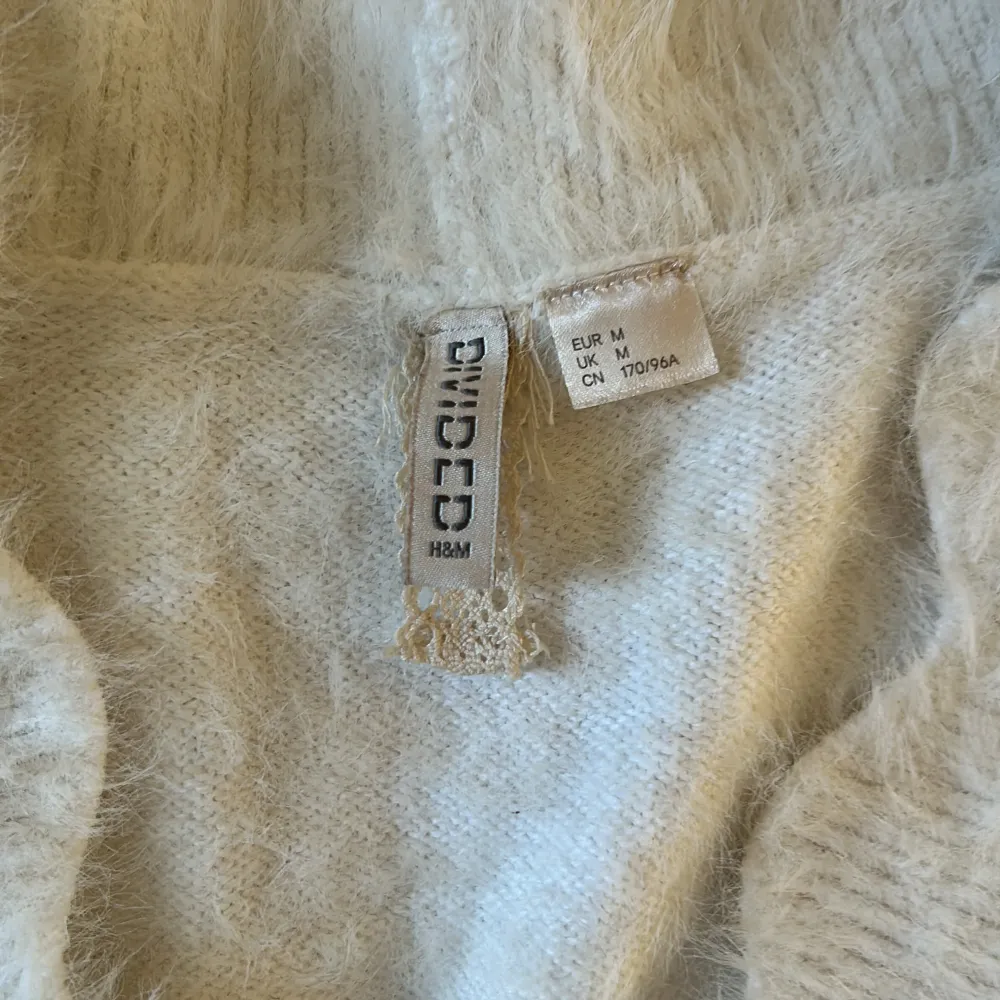 Säljer en supermjuk och fluffig vit tröja från H&M. Den har en v-ringad design och är perfekt för kyliga dagar. Tröjan är långärmad och har en ribbad kant vid ärmslut och nederkant. Perfekt för både vardag och mysiga hemmakvällar! 🧡. Tröjor & Koftor.