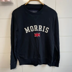 Marinblå tröja från Morris - Säljer en snygg marinblå tröja från Morris med text och en brittisk flagga på framsidan. Tröjan är i storlek medium. Frågor och funderingar? Hör bara av dig