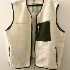 Teddyväst - Teddyväst med grön ficka och rundad hals. Verkligen så fin och gosig nu till höst. Storlek xxl, normal i storleken, perfekt med hoodie under eller stickad tröja 