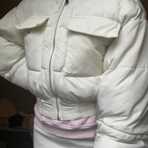 Vit pufferjacka från NA-KD - Säljer en snygg vit pufferjacka från NA-KD. Den är perfekt för kyliga dagar med sin puffiga design och dragkedja framtill. Jackan har långa ärmar och praktiska fickor med knappar. Saknad däremot en knapp på ena fickan, därav priset. Den är i ok skick med några mindre fläckar. 