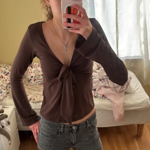 Brun långärmad topp med knyt - Säljer en snygg brun långärmad topp (från gina) med v-ringning och knyt framtill. Perfekt för höst och vår. Passar bra till både jeans och kjol! Använd bara en gång så den är i bra skick. Säljer då den ej kommer till användning.🥰 Storlek:S 