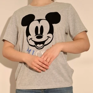 Grå t-shirt med musse pigg motiv - Grå t-shirt med Musse pigg motiv.  (Sista bilden visar tröjans material)