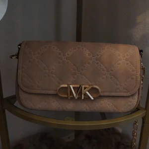 Beige axelväska med logotypdetalj - Snygg beige axelväska med quiltat mönster och en elegant logotypdetalj på framsidan. Väskan har en kedjerem och praktisk dragkedja inuti för säker förvaring. Perfekt för att ge din outfit en stilfull touch. Nypris är 3700