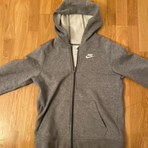Vanlig mörk grå Nike kofta - Säljer en mörk grå Nike kofta. Den har används runt 2 gånger och har blivit liten på mig. Storleken är 158-170. !jag har lagt storlek beskrivningen S för att det går ej att lägga barn storlek!