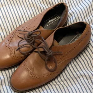 Bruna skor från Retroo - Snygga bruna brogues i skinn från Retroo med klassisk snörning och dekorativa perforeringar. Perfekta för en stilren look. Köpta second hand för 200kr
