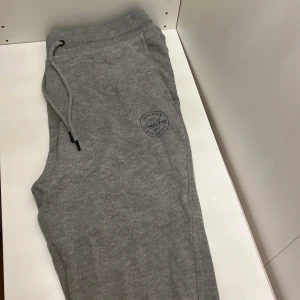 Grå mjukisbyxor från Jack & Jones - Snygga och bekväma grå mjukisbyxor från Jack & Jones. De har en elastisk midja med snörning och praktiska sidofickor. Perfekta för en avslappnad stil. Nypris 399.95kr