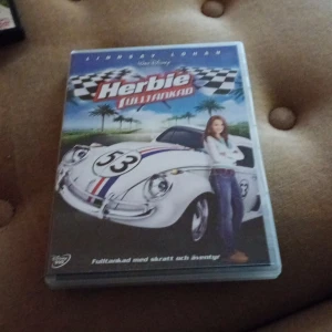 Herbie: Fulltankad DVD - DVD-film 'Herbie: Fulltankad' från Walt Disney. Omslaget visar en vit bil med nummer 53 och en person stående bredvid. Filmen är en del av Herbie-serien och innehåller humor och äventyr.