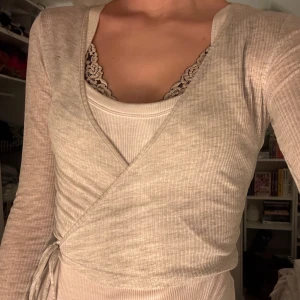 Beige omlottopp - INTRESSEKOLL Snygg beige omlottopp med ribbad textur och knytning i sidan. Perfekt för lager-på-lager-stil och ger en elegant touch till din outfit. Skriv vid intresse