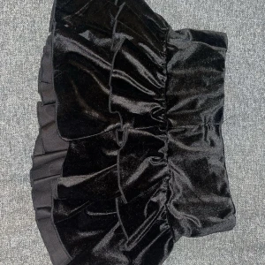 Svart sammetskjol med volang - Snygg svart kortkjol i sammet med volangdetaljer. Kjolen har en elastisk midja för bekväm passform.