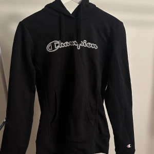 Svart hoodie från Champion - Superfin svart champion hoodie med tryck🖤 Sitter som en S/XS mer än som en M!! Fint skick och super mjukt tyg.   Tveka inte att skriva vid frågor✨