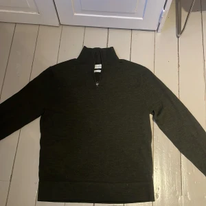 Mörkgrön stickad half-zip i merinoull från These Glory Days - Säljer en stilren mörkgrön tröja i 100% merinoull från These Glory Days. Tröjan är en half-zip med långa ärmar. Perfekt för kyligare dagar med sin mjuka och varma känsla. Passar till många outfits.  Nypris: 900