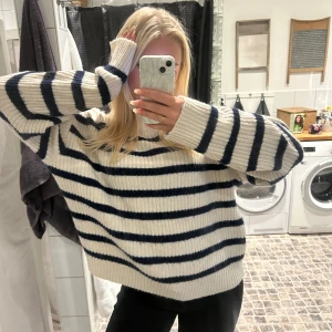 Randig stickad tröja - Mysig stickad tröja i vitt med marinblå ränder. Tröjan har en avslappnad passform och långa ärmar, perfekt för kyligare dagar. Den ribbade strukturen ger en extra touch av stil.