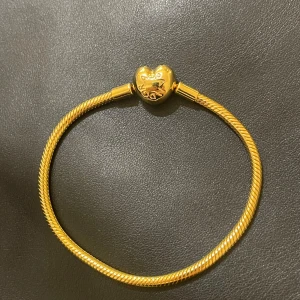Guldarmband från Pandora - Elegant guldarmband från Pandora med ett hjärtformat lås. Perfekt för att bära ensamt eller med berlocker. Kommer med äkthetscertifikat och presentförpackning. Armbandet är helt nytt då det aldrig har använts eftersom armbandet har varit för stort från början. 