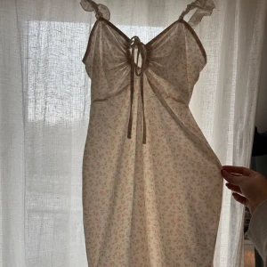 Blommig klänning från NLY Trend - Söt blommig klänning från NLY Trend i ljusa färger. Klänningen har smala axelband och en knytning framtill. Perfekt för varma dagar med sin lätta och luftiga design.