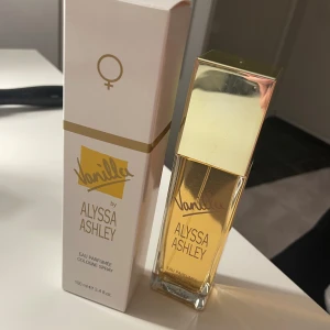 Vanilla Eau Parfumée Cologne Spray från Alyssa Ashley - En elegant parfym med en varm vaniljdoft från Alyssa Ashley. Flaskan är rektangulär med en gyllene kork och rymmer 100 ml. Förpackningen är stilren i vitt och guld med en feminin symbol. Helt ny fick dubbel i julklapp 