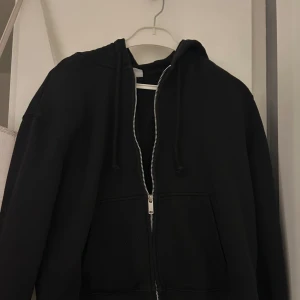 Svart hoodie med dragkedja/ svart ziphoodie - Säljer en klassisk svart hoodie med dragkedja och luva. Perfekt för en avslappnad stil. Använd kanske max 3 gånger och ser ut som ny utan defekter. Hör gärna av till mig för frågor eller så💕