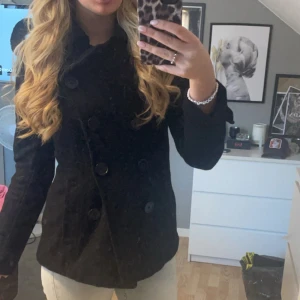 Svart kappa med knappar - Snygg svart kappa med stora knappar framtill. Perfekt för kyligare dagar med sin stilrena design och långa ärmar. Passar bra till både jeans och klänning.