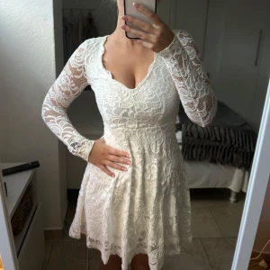 Vit spetsklänning med lång ärm - Elegant vit klänning i spets med långärmad design och v-ringad hals. Perfekt för speciella tillfällen med sin romantiska stil och fina detaljer.