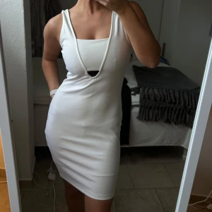 Vit ärmlös klänning - Snygg vit ärmlös klänning med djup v-ringning. Den har en tight passform som framhäver figuren. Perfekt för en stilren och elegant look.