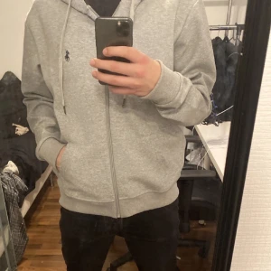Grå hoodie från Polo Ralph Lauren - Säljer en stilren grå hoodie från Polo Ralph Lauren med dragkedja och det klassiska logotypbroderiet på bröstet. Perfekt för en avslappnad stil. Kom privat för mer information! Passar S/M Köpt från Snowbox för 850 kr