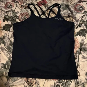 Svart träningslinne från Gavelo - Snygg svart träningslinne från Gavelo med korsade axelband. Perfekt för träning eller en avslappnad dag. Enkel och stilren design med liten logga framtill.