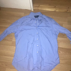 Blå skjorta från Polo Ralph Lauren - Snygg blå skjorta från Polo Ralph Lauren i klassisk passform. Skjortan har långa ärmar och knappar framtill. Perfekt för en stilren look.