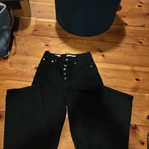 Svarta jeans med knappar - Snygga svarta jeans med hög midja och knappgylf. Perfekta för en stilren look. Passar till många olika outfits och tillfällen.