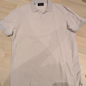 Beige pikétröja från Selected Homme - Snygg beige pikétröja från Selected Homme i storlek M. Perfekt för en stilren och avslappnad look. Tröjan har korta ärmar och en krage utan knappar.