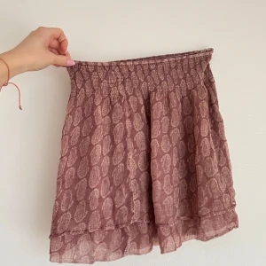 Rosa kjol  - Säljer en söt rosa kjol med ett subtilt mönster och elastisk midja. Kjolen har en lätt volangdetalj vid fållen som ger en fin rörelse. Perfekt för en avslappnad och stilfull look.