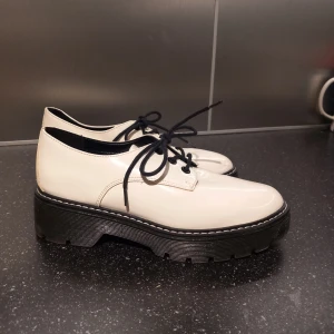 Vita skor - Snygga vita snörskor med en robust svart sula och svarta snören. Skorna har en blank yta. Helt oanvända. 