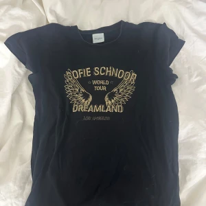 Svart t-shirt från Sofie Schnoor - Snygg svart t-shirt från Sofie Schnoor med tryck i guld och texten 'World Tour Dreamland Los Angeles'. Perfekt för en cool och avslappnad stil.