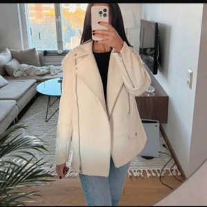 Vit kappa med dragkedja - Säljer en stilren vit kappa med dragkedja och krage. Jackan har en modern design med långa ärmar och en asymmetrisk dragkedja framtill. Perfekt för att hålla stilen i kyligare väder.