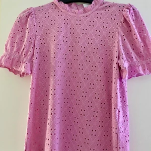 Rosa blus från VILA - Söt rosa blus från VILA med korta puffärmar och ett vackert broderat mönster. Blusen har en rund halsringning och en liten öppning i ryggen. Aldrig använd, ny utan prislapp.