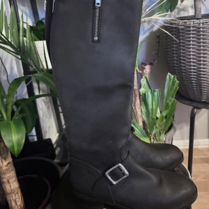 Svarta stövlar från Urban Project - Snygga svarta stövlar från Urban Project med dragkedja och spänne. Tillverkade i Spanien med stilren design. Perfekta för en trendig look.
