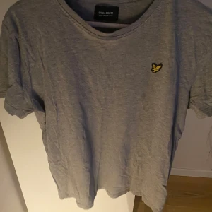 Grå t-shirt från Lyle & Scott - Säljer en stilren grå t-shirt från Lyle & Scott med deras ikoniska logga på bröstet. Perfekt för en avslappnad look.