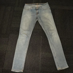 Ljusblå jeans från Nudie Jeans - Snygga ljusblå jeans från Nudie Jeans med en klassisk femficksdesign och orange sömmar. De har en knappgylf och är i en straight passform. Perfekta för en avslappnad stil. Sydda själva mellan bena inget som syns men drar ner på priset. Nypris 1200. W27 L32