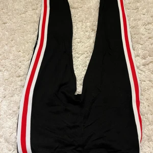 Svarta byxor med rödvita ränder - Ett par slim, svarta mjukis byxor med snygga rödvita ränder på sidorna! Använt fåtal gånger.