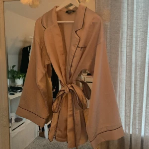 Morgonrock  - Morgonrock i stl 36. Kort och slutar under rumpan på mig som är 165. Snygga utsvängda armar. Rosa beige färg med svarta detaljer.